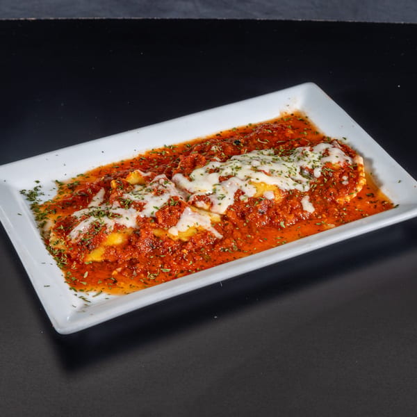 Baked ravioli covered in red sauce, melted mozzarella cheese, and green herbs on a white rectangular plate.