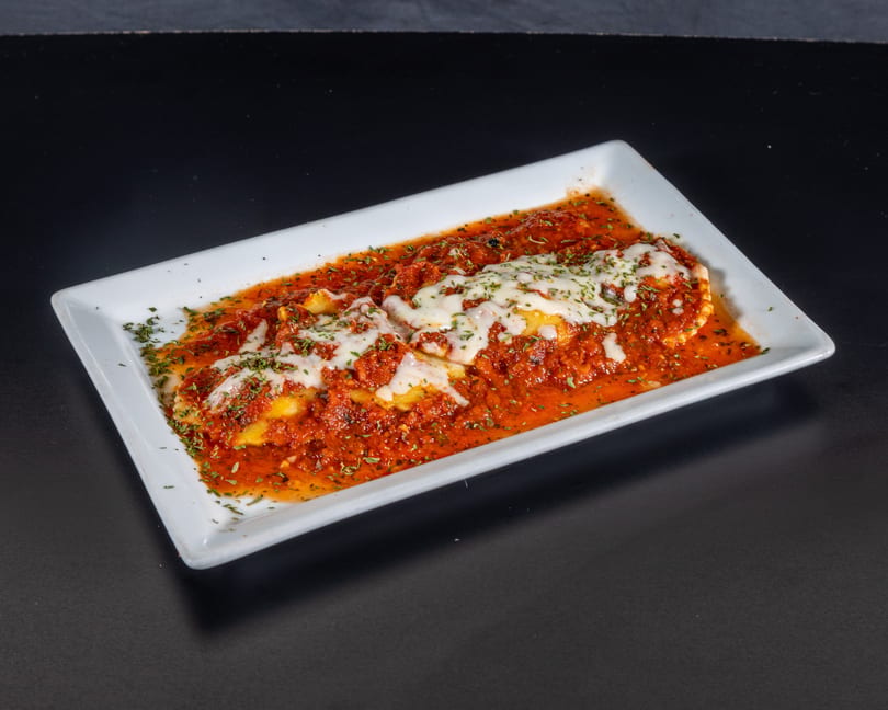 Baked ravioli covered in red sauce, melted mozzarella cheese, and green herbs on a white rectangular plate.