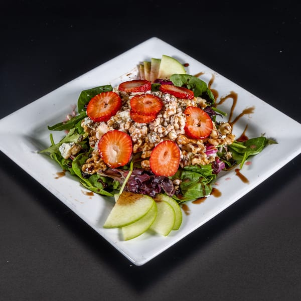 A fresh salad with strawberries, walnuts, blue cheese, and apple slices on a white plate.