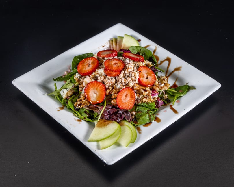 A fresh salad with strawberries, walnuts, blue cheese, and apple slices on a white plate.