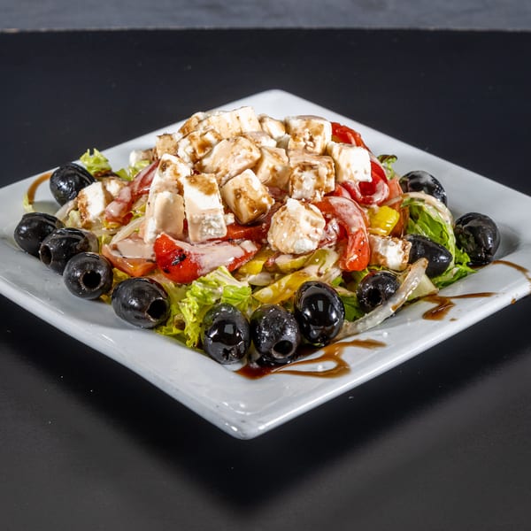 A fresh salad with lettuce, tomatoes, bell peppers, feta cheese, and black olives on a white plate.