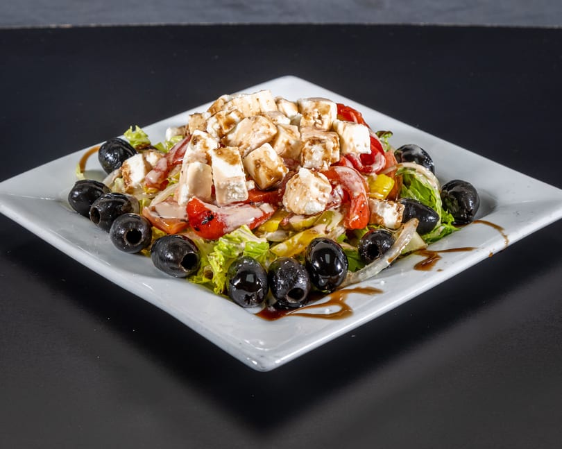 A fresh salad with lettuce, tomatoes, bell peppers, feta cheese, and black olives on a white plate.