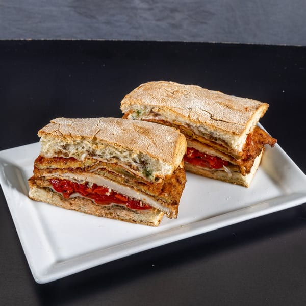 Two hearty sandwiches with fried cutlets, roasted red peppers, and cheese on ciabatta bread.