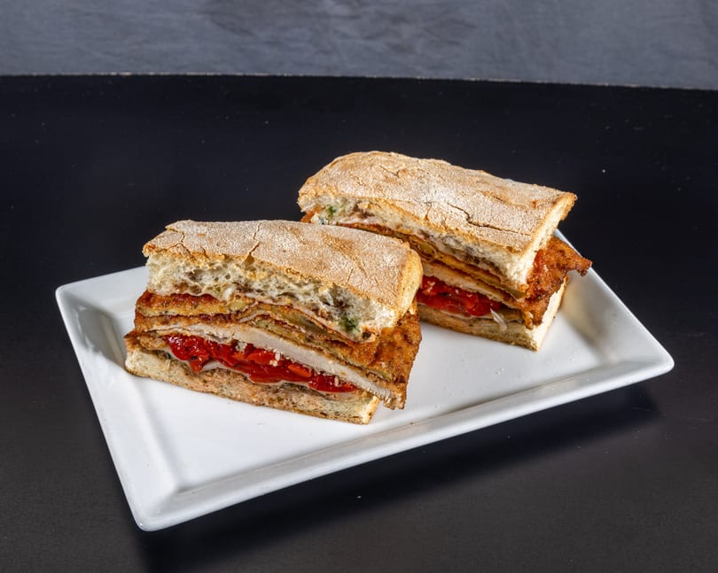 Two hearty sandwiches with fried cutlets, roasted red peppers, and cheese on ciabatta bread.