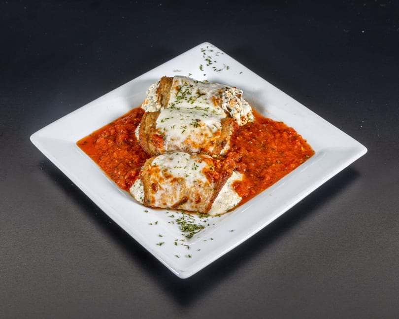 Two cheese-covered eggplant parmesan rolls in a rich red sauce, garnished with parsley on a white plate.
