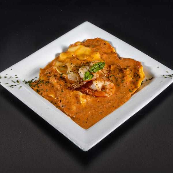 Shrimp ravioli in a creamy red sauce, garnished with fresh basil and herbs on a white plate.