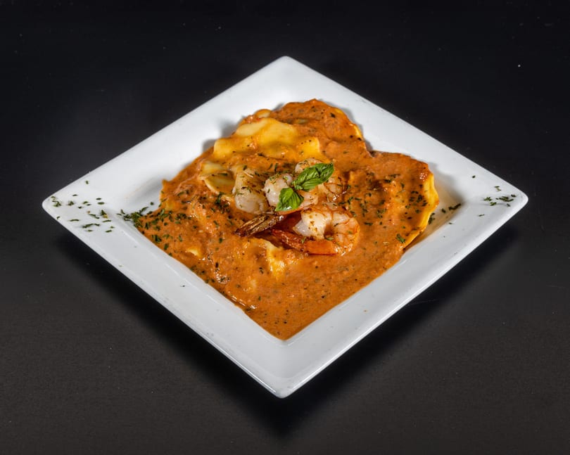 Shrimp ravioli in a creamy red sauce, garnished with fresh basil and herbs on a white plate.